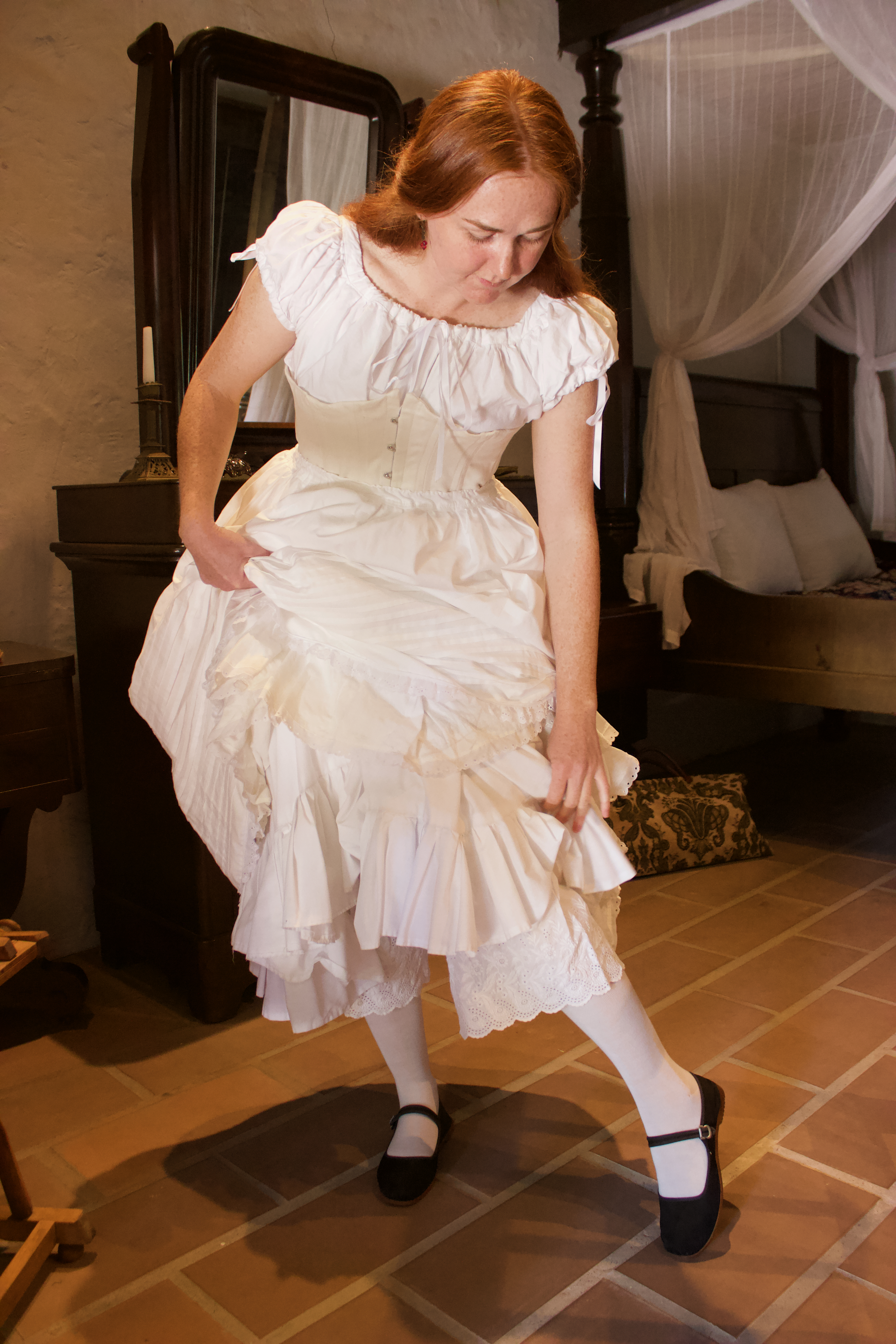 Photo of a woman in period undergarments holding up her petticoats to look at her shoes